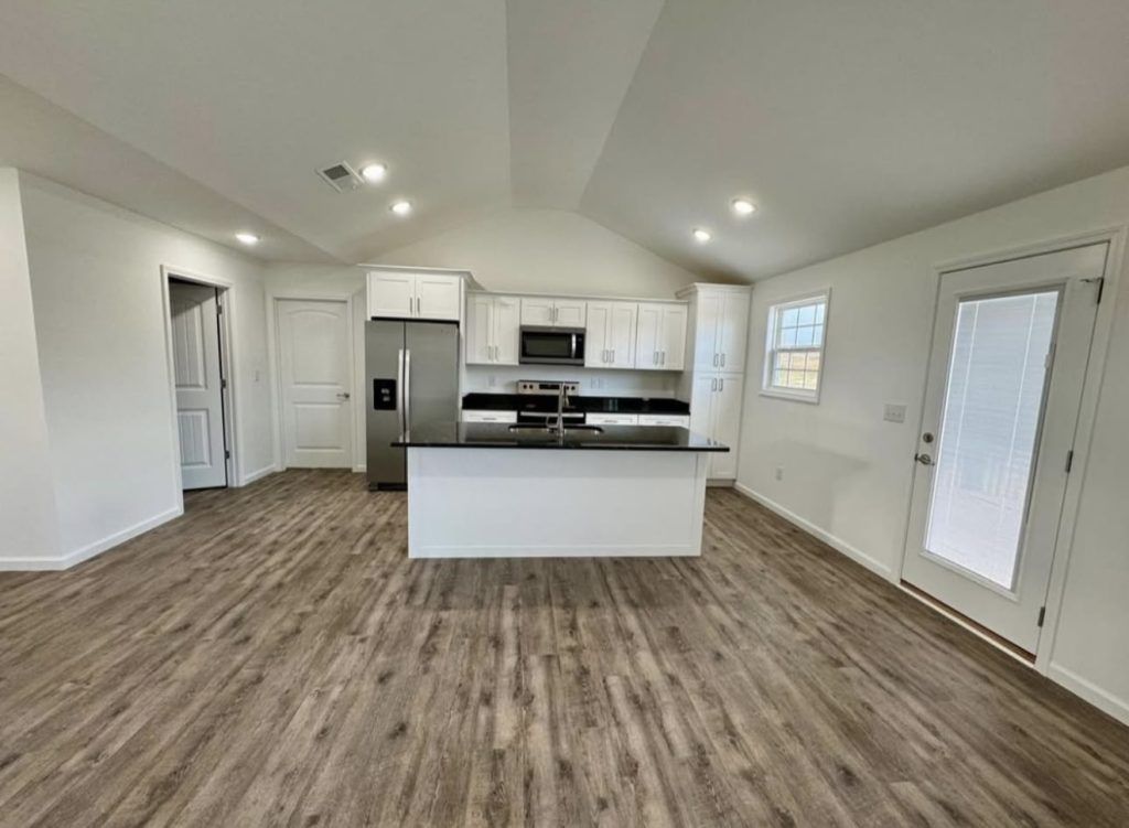 A modern, open-concept kitchen and living area featuring white cabinets, stainless steel appliances, and wood flooring.