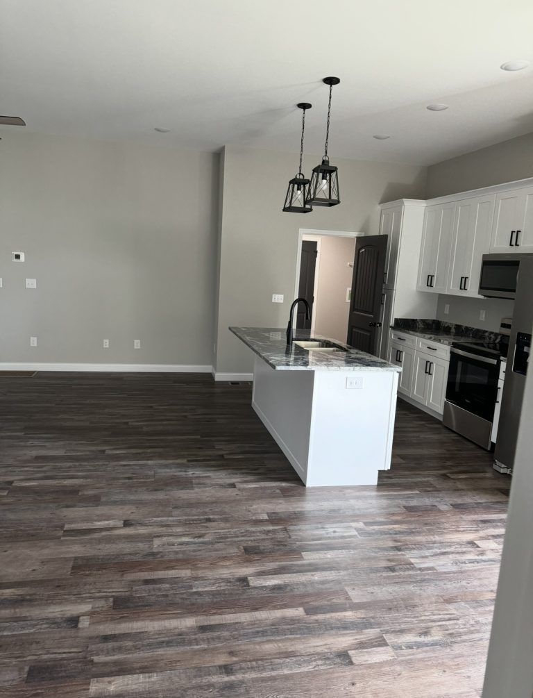 An open-plan kitchen with white cabinets, a central island with a faucet, and dark wood-look flooring.