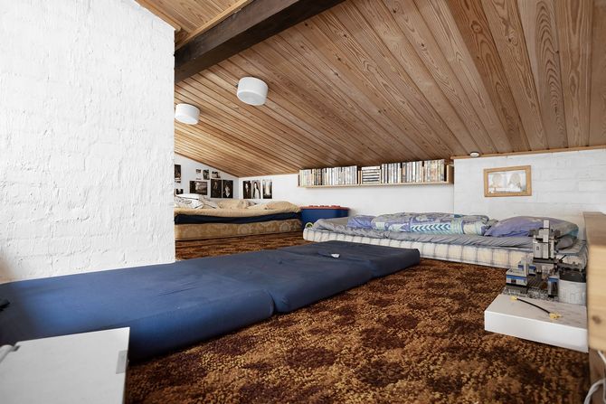 Retro bedroom with wood-paneled slanted ceiling, blue bed, patterned carpet, and low sofa seating