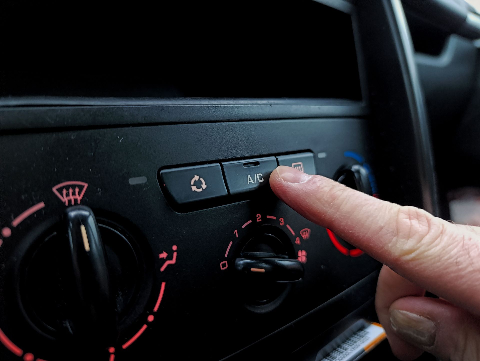 Finger pressing car climate control buttons on dashboard with red-lit dials