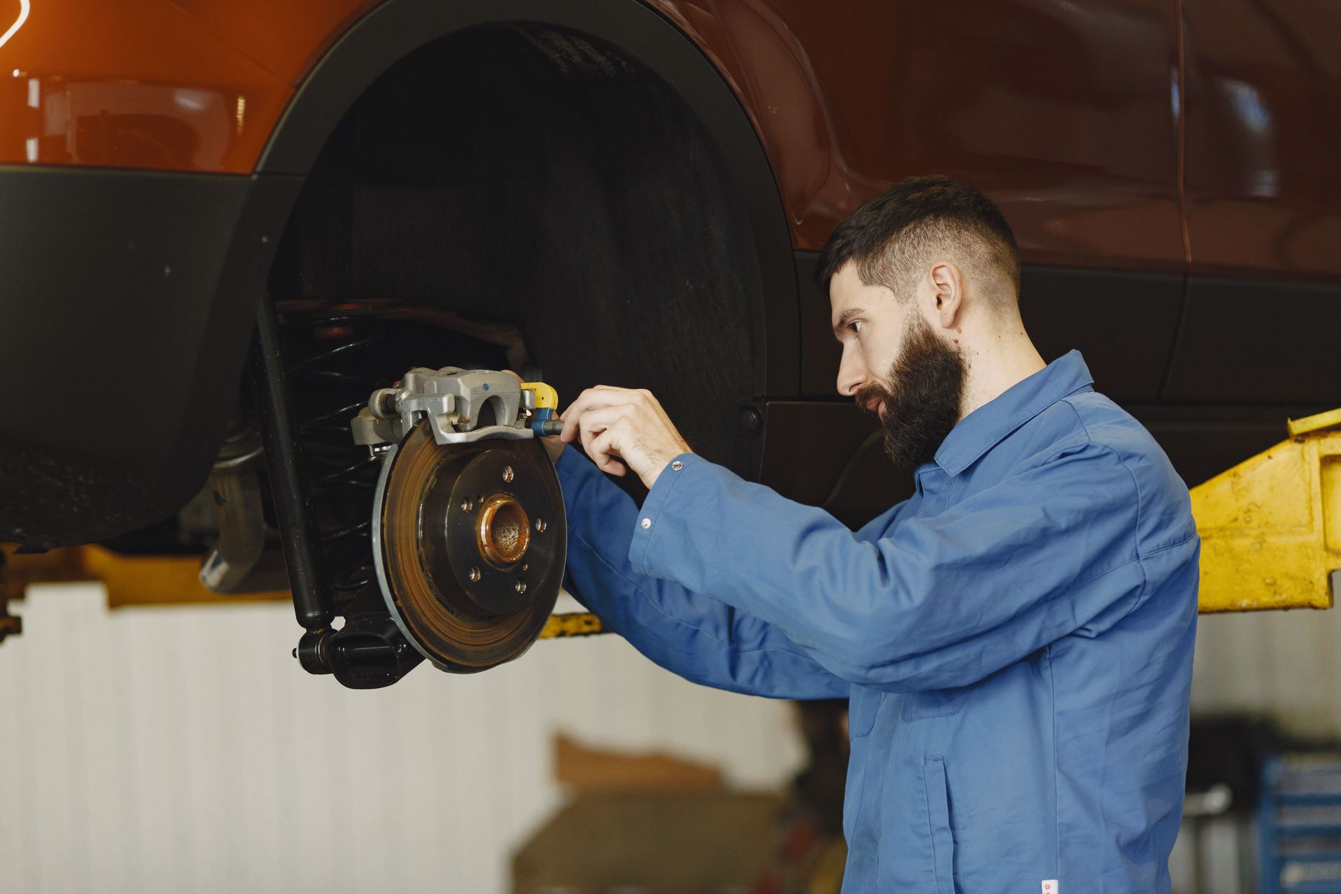 Mechanic in blue coveralls inspecting a car’s brake assembly in a workshop