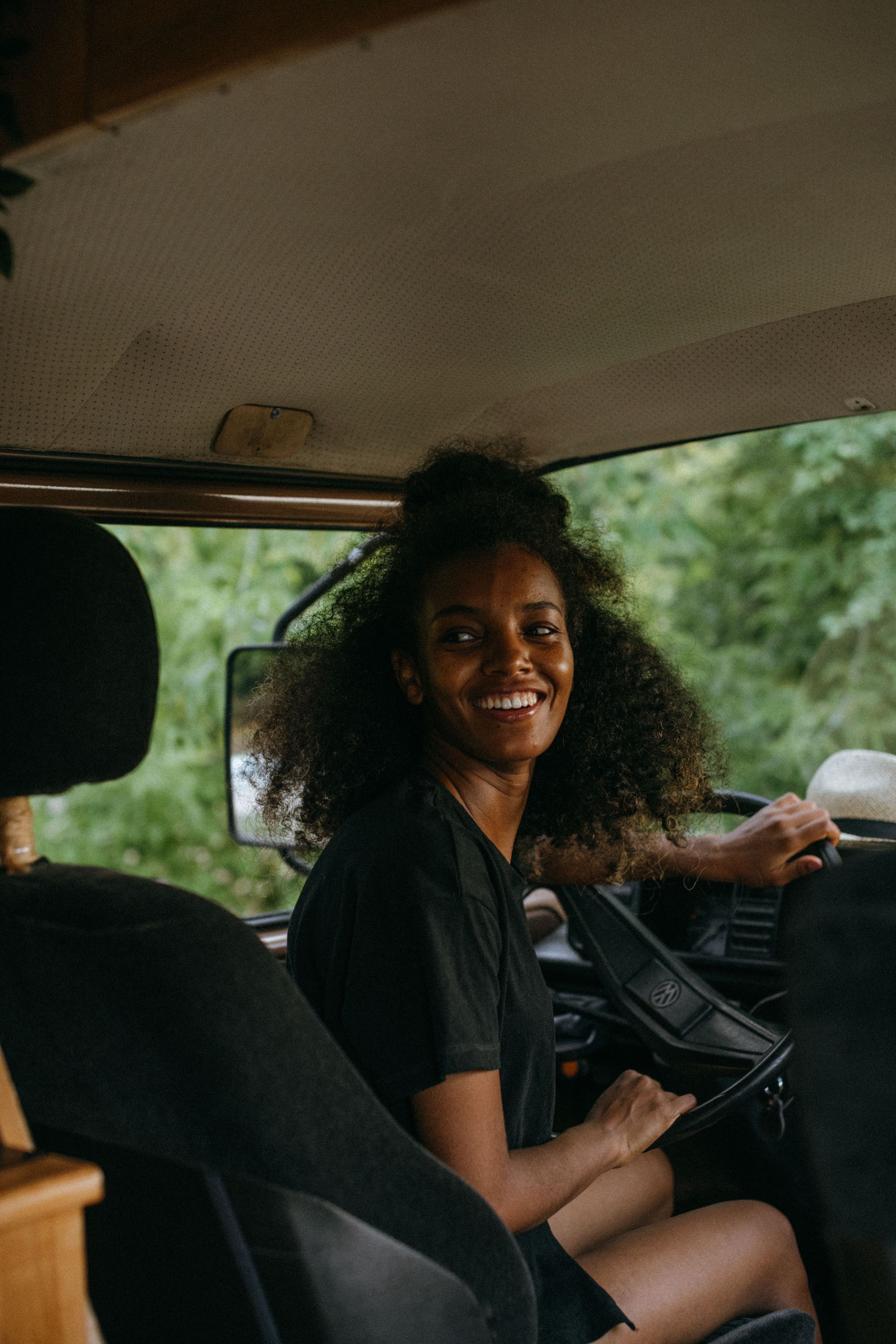 Woman smiling in a car, seated in the driver’s seat with greenery outside the window.