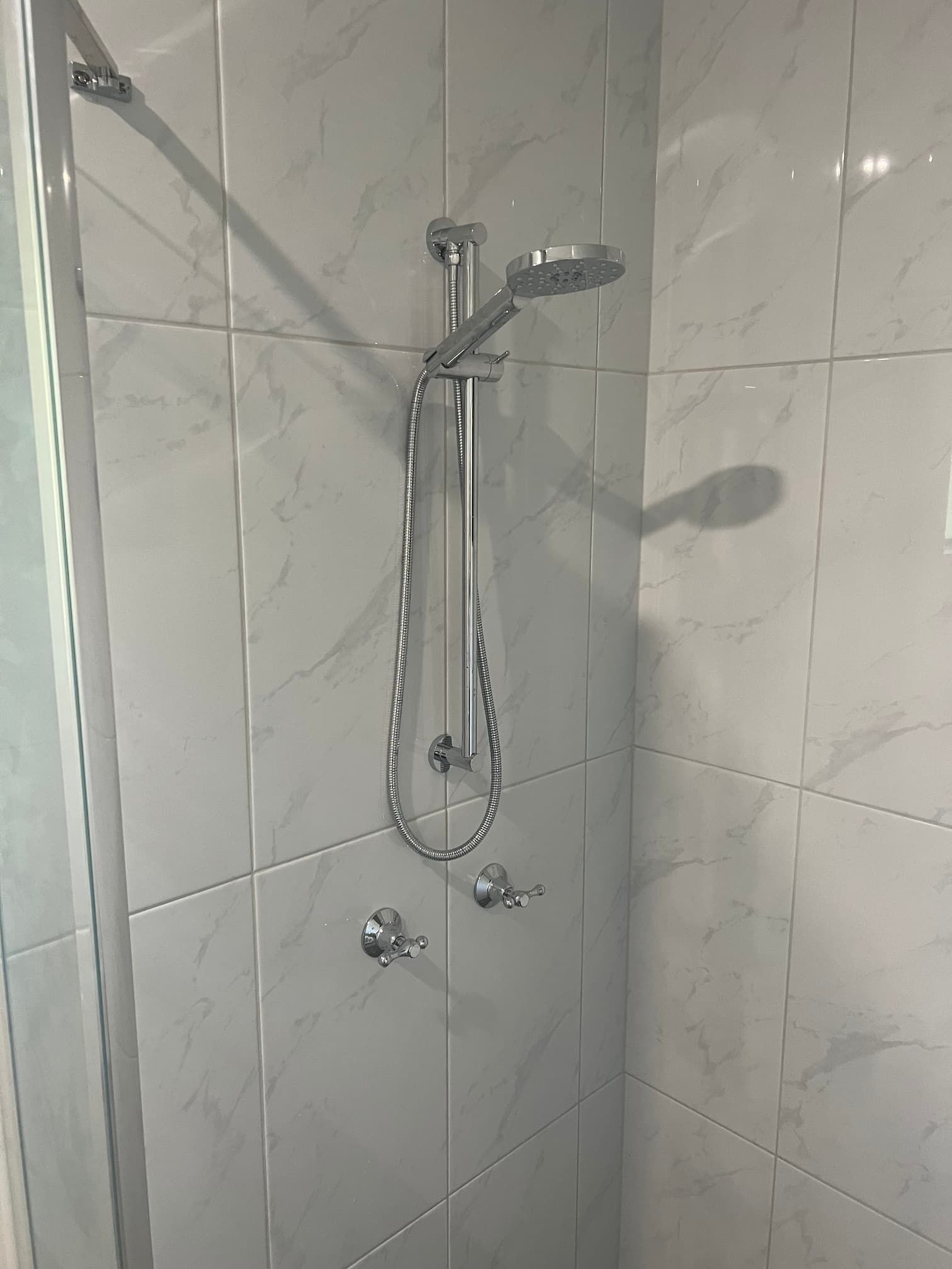 Shower with chrome fixtures on white marble-look tile.
