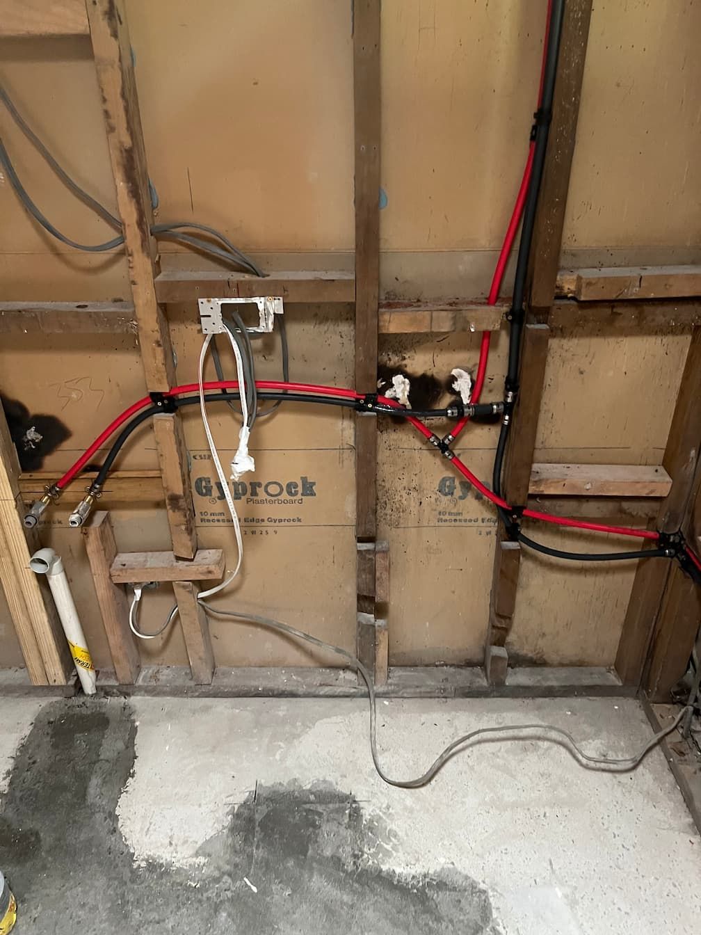 Exposed wall with plumbing and electrical wiring. Red pipes, black wiring, and drywall.