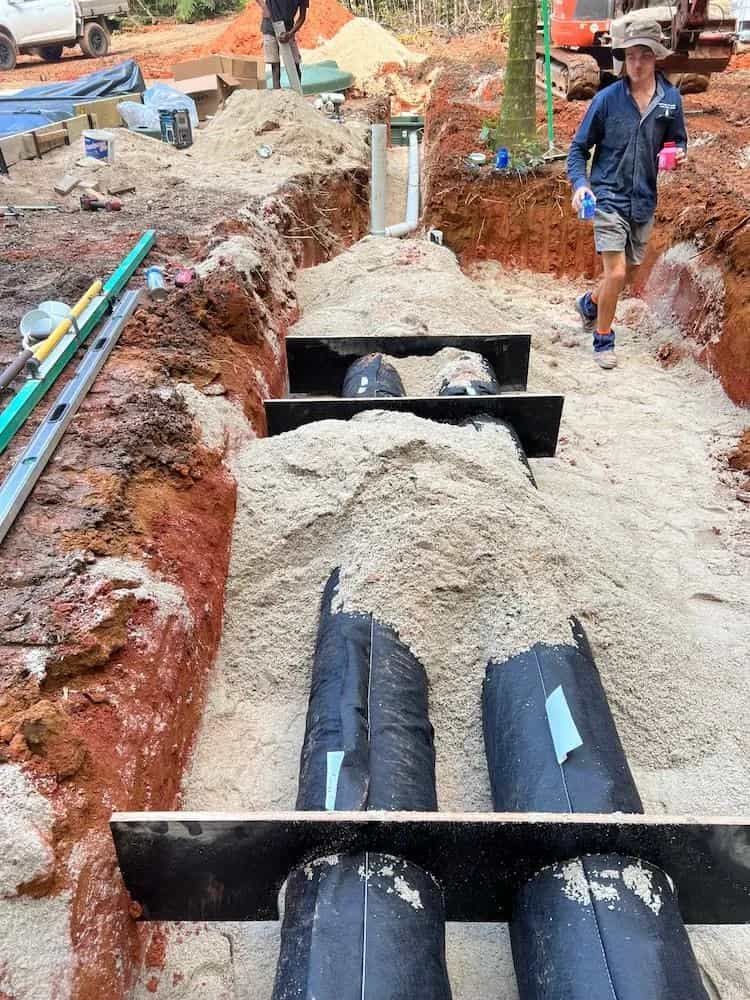 Construction site: Trench with black pipes, sand, and workers.