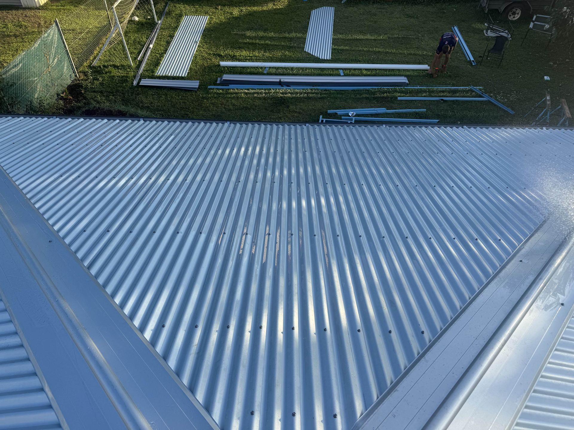 Corrugated metal roof with adjacent materials laid out on grass.