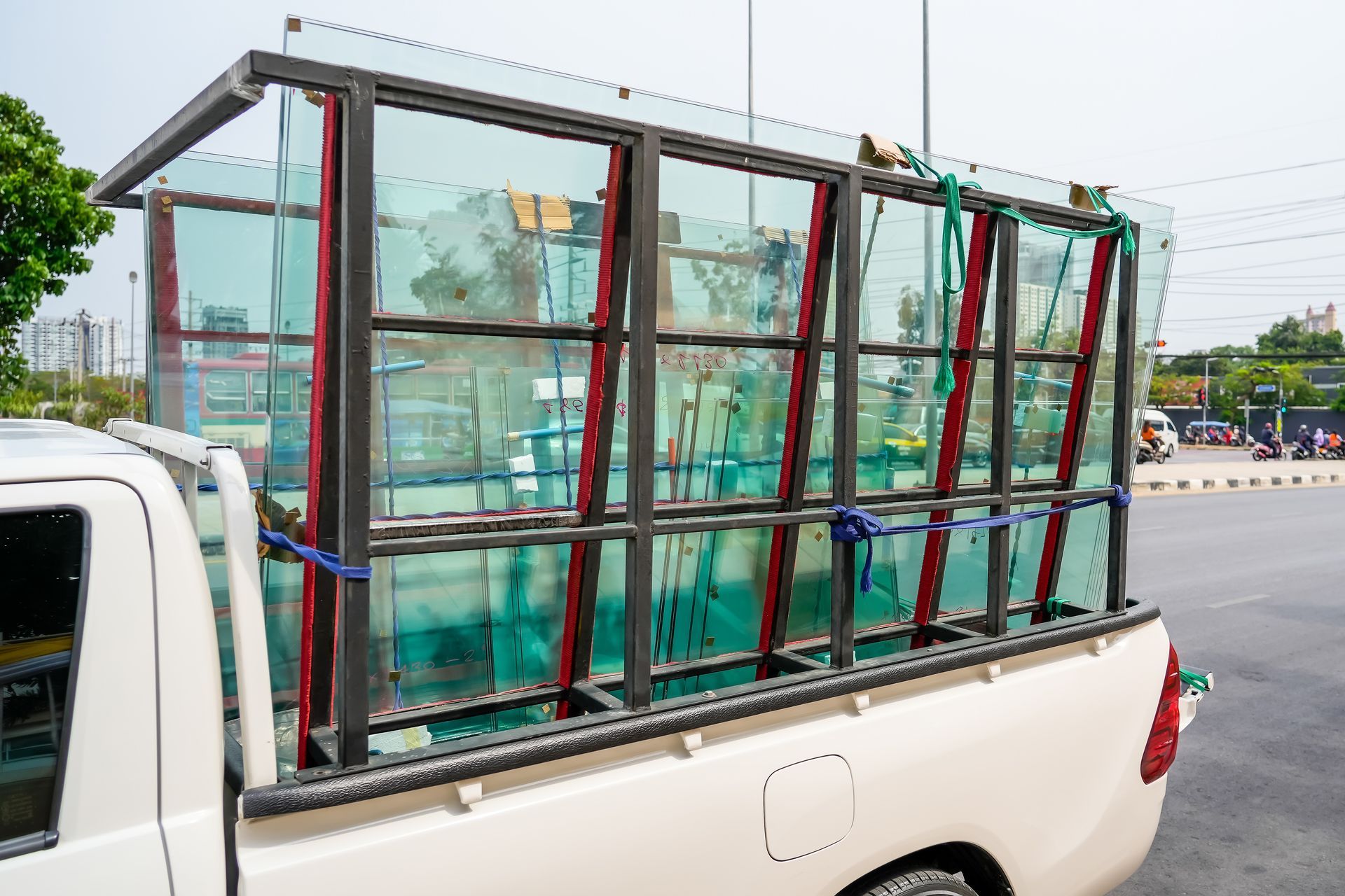 White pickup truck bed carrying large panes of green glass secured in a metal frame.