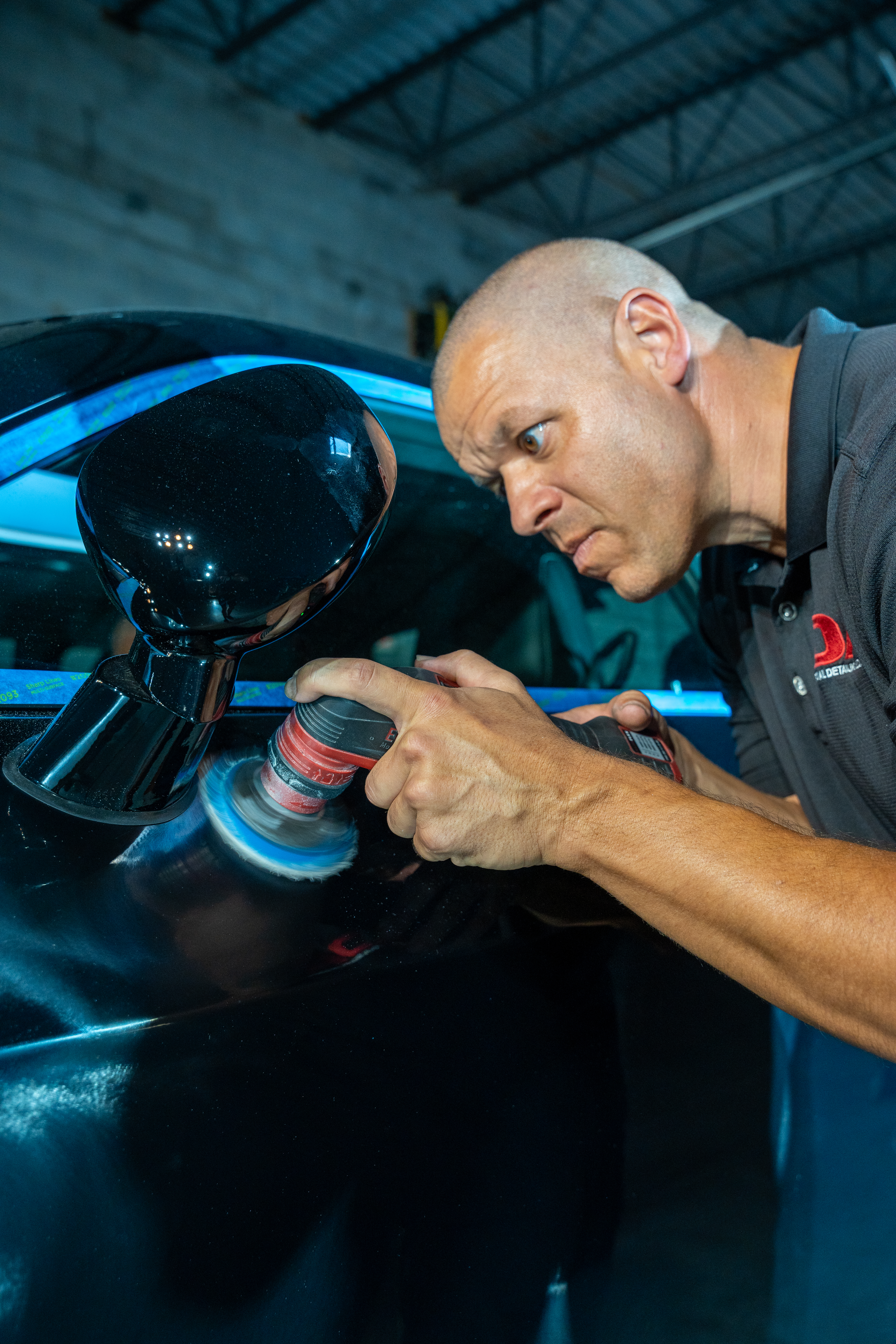 A man is polishing a car with a machine in a garage.