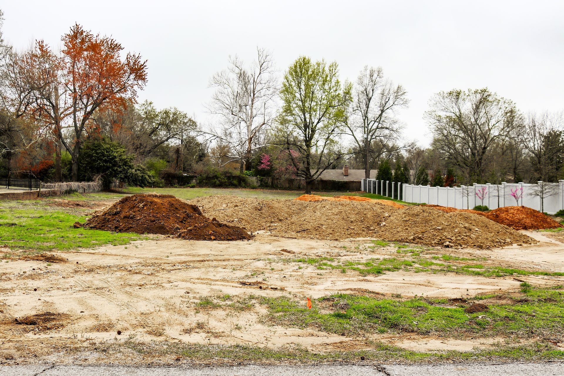 A dirt field with a white fence and trees in the background.