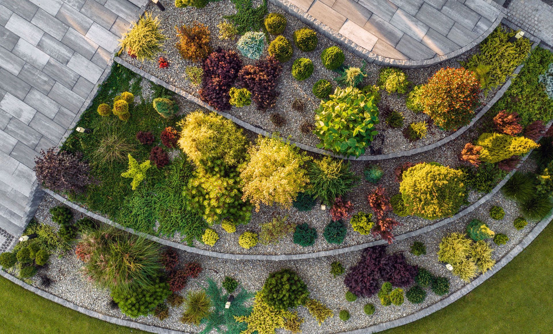 Curved rooftop garden with colorful plants, shrubs, and gravel borders beside gray roof tiles