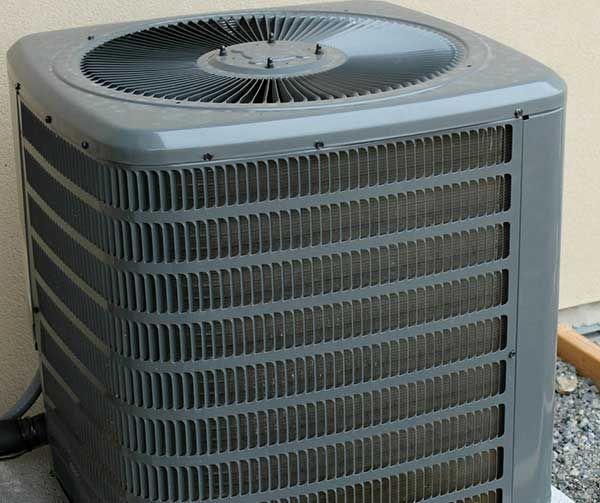 Outdoor central air conditioning unit beside a wall, gray metal with top fan grille