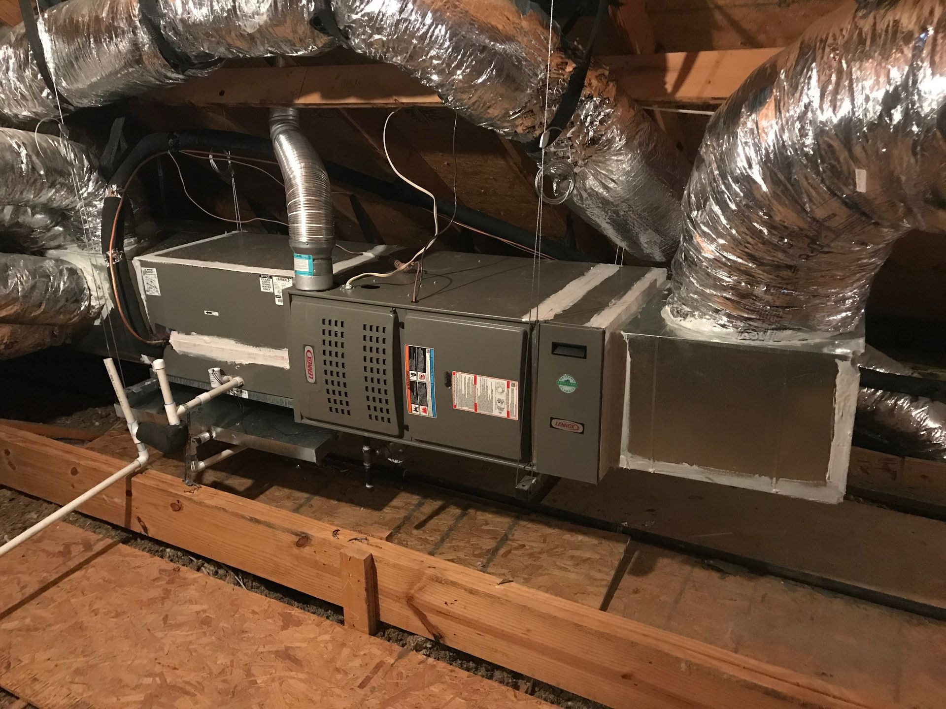 HVAC furnace and ductwork in an attic, with insulated flexible vents and exposed wooden rafters
