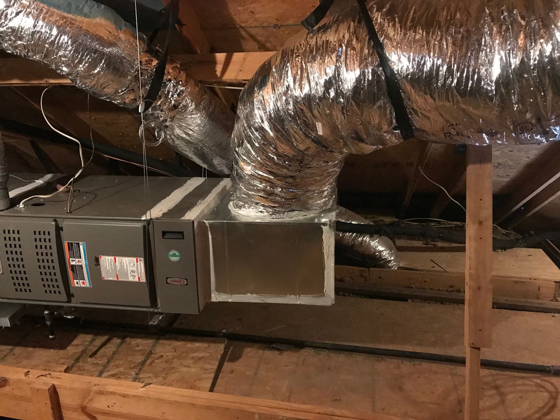Attic HVAC ducts and a metal vent box with foil insulation and exposed wooden beams