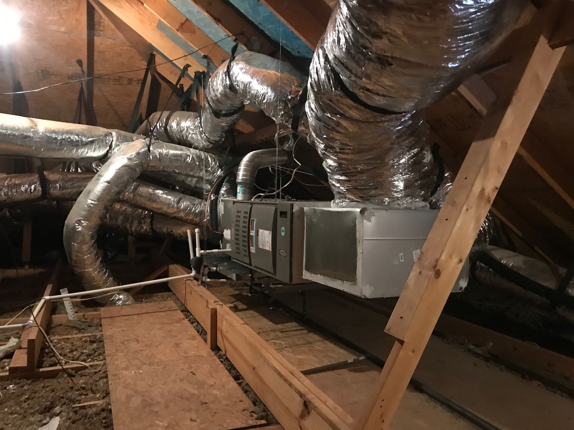 Attic HVAC system with silver ductwork, metal unit, and wooden beams overhead