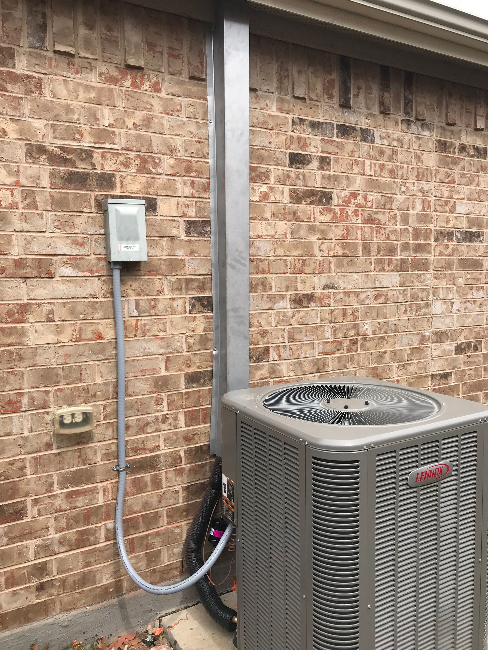 Outdoor air conditioner unit beside a brick wall with a metal conduit and electrical box