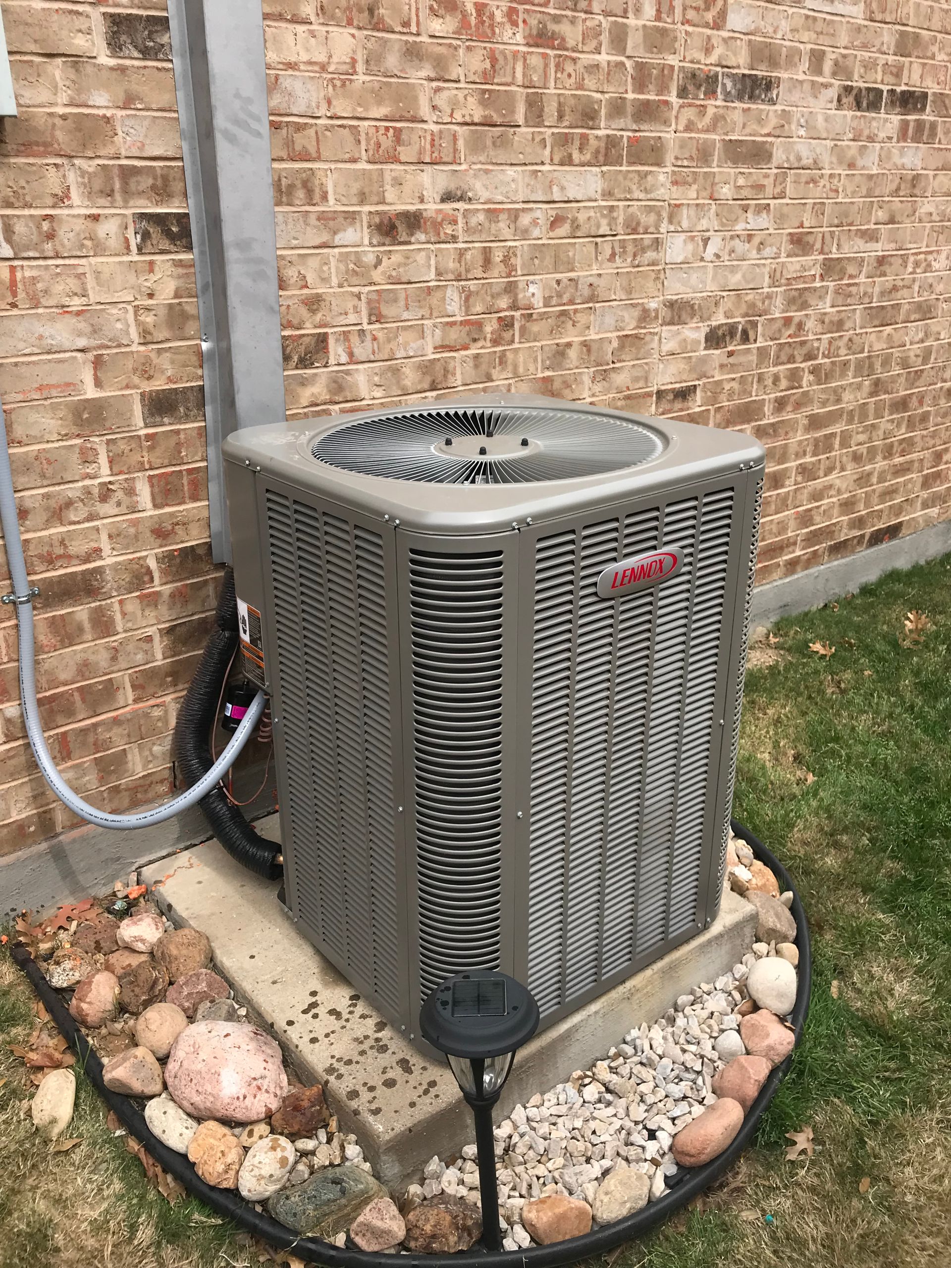 Outdoor air conditioner unit beside a brick wall on a stone border