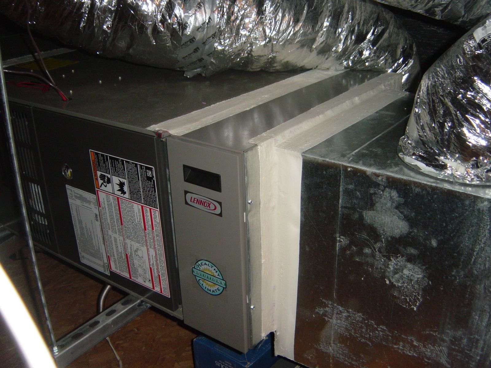 Metal HVAC ductwork in a ceiling crawlspace, with reflective insulation and a beige unit between ducts