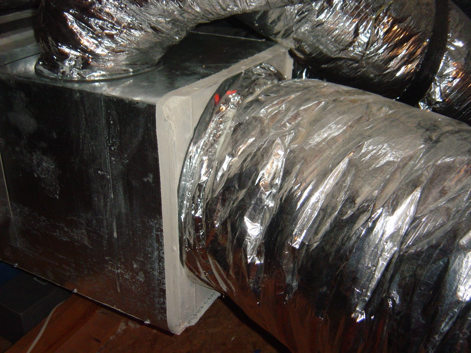 Silver insulated duct connected to a rectangular HVAC vent box.