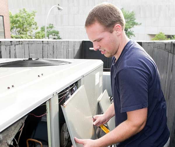 Technician removing a panel from an outdoor HVAC unit on a rooftop or patio