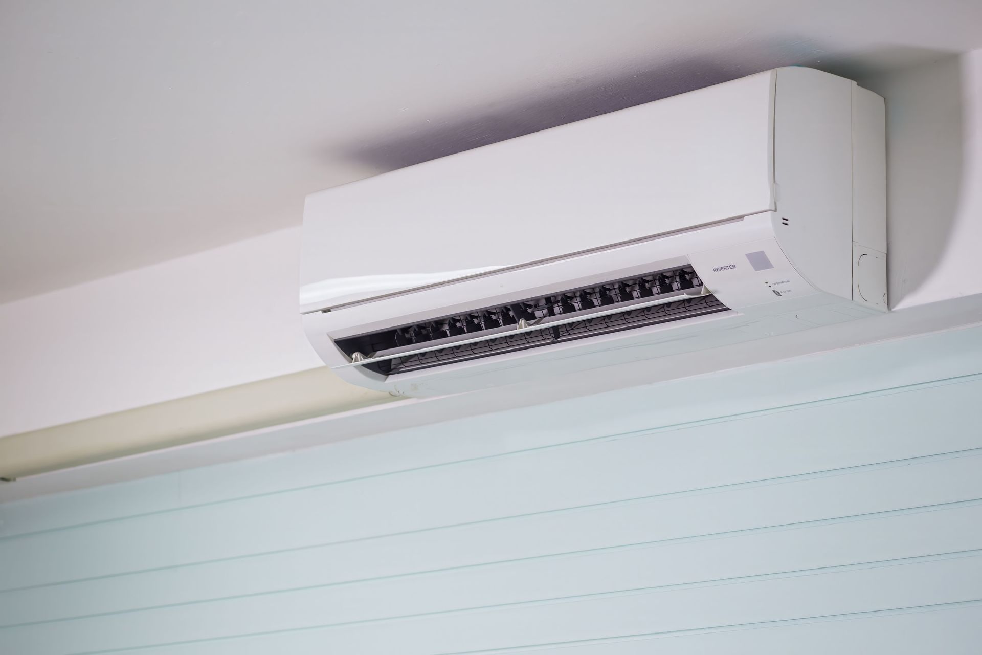 Wall-mounted white air conditioner above a room window or wall paneling