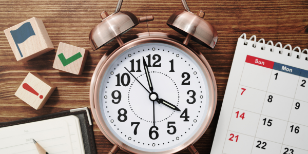 Alarm clock beside calendar, wooden blocks, and pen on a desk