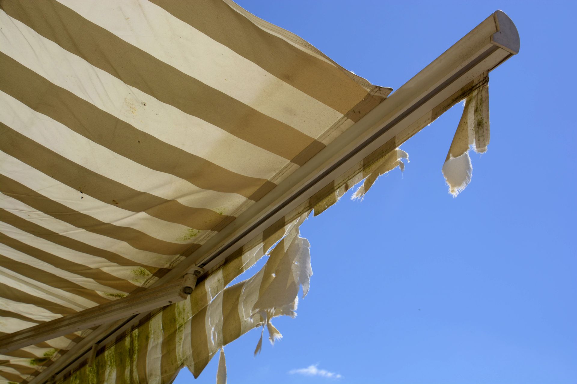 yellow striped awning that is dirty, torn and broken
