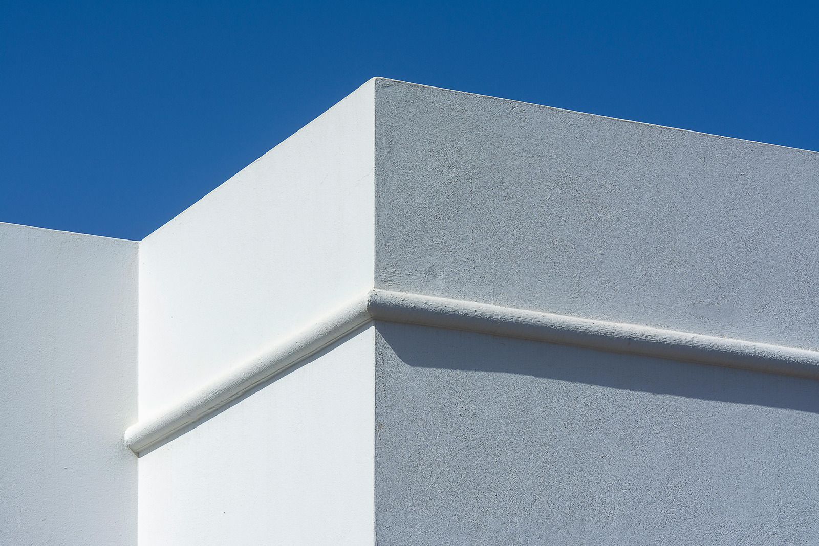 A bright white building corner with textured walls and a horizontal decorative molding against a clear blue sky.