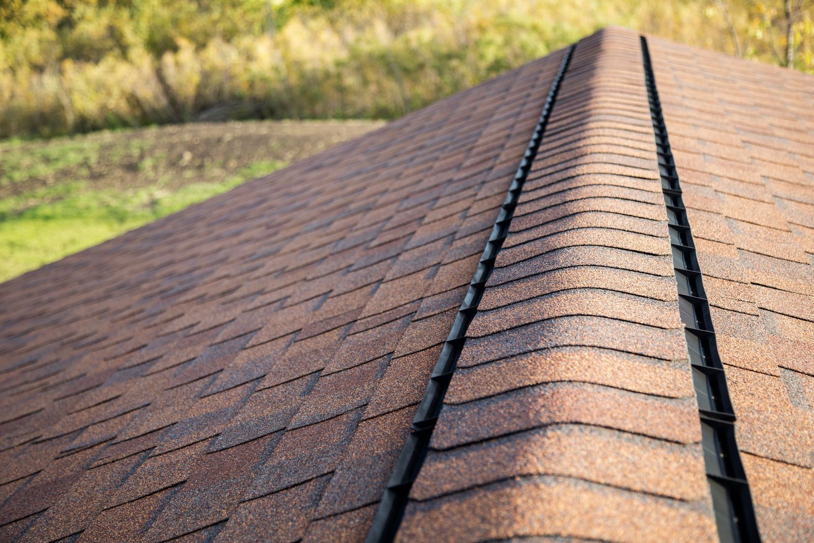 A close-up, angled view of a brown shingled roof with a black ridge vent installed along the peak.