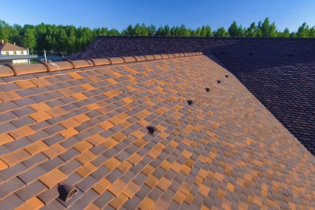 A roof featuring a pattern of alternating brown and orange clay tiles, with small vent caps installed along the slope.