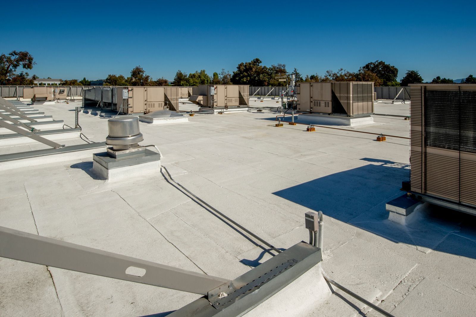 A flat commercial rooftop on a sunny day with multiple HVAC units and ventilation equipment.