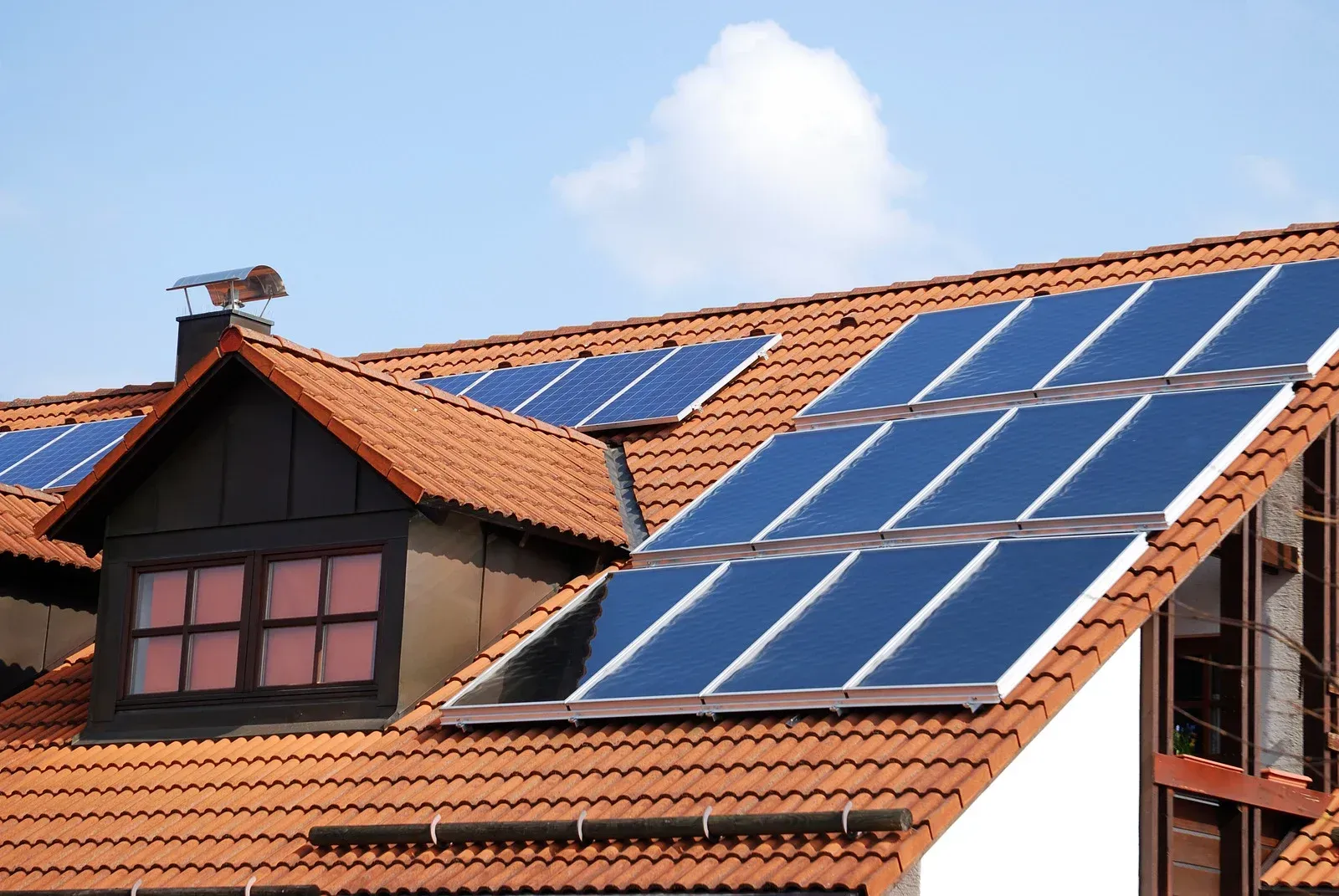 A terracotta-tiled roof featuring multiple installed solar panels against a clear blue sky.