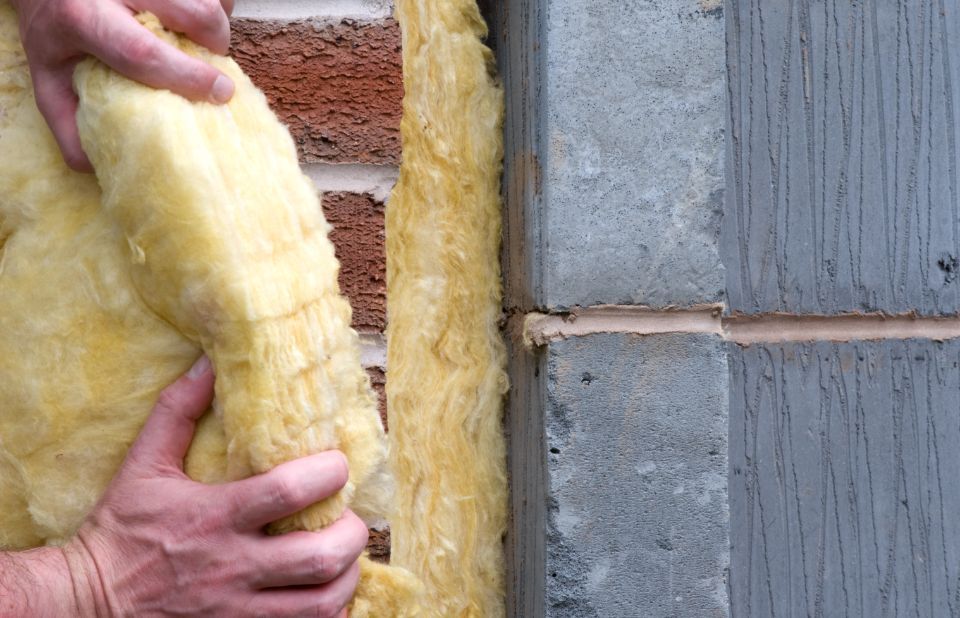 isolante in fibra di vetro gialla nell’intercapedine di una parete, accanto a blocchi di cemento e a una struttura in legno