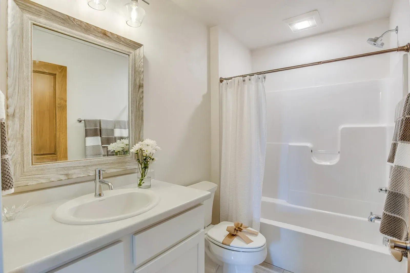 White bathroom with a framed mirror, white sink, and shower/tub combo; neutral decor.