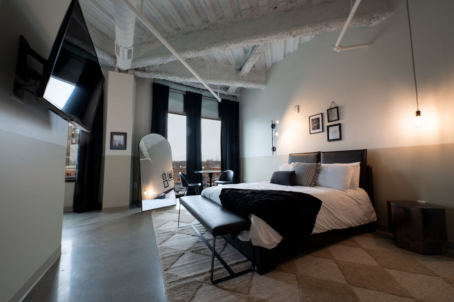 Modern bedroom with exposed beams, black-and-white bedding, wall art, and large windows