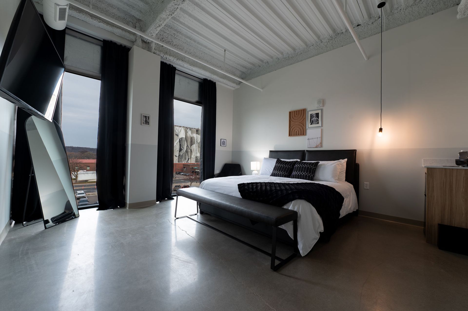 Modern bedroom with black-and-white decor, large windows, a bed, and a hanging pendant light