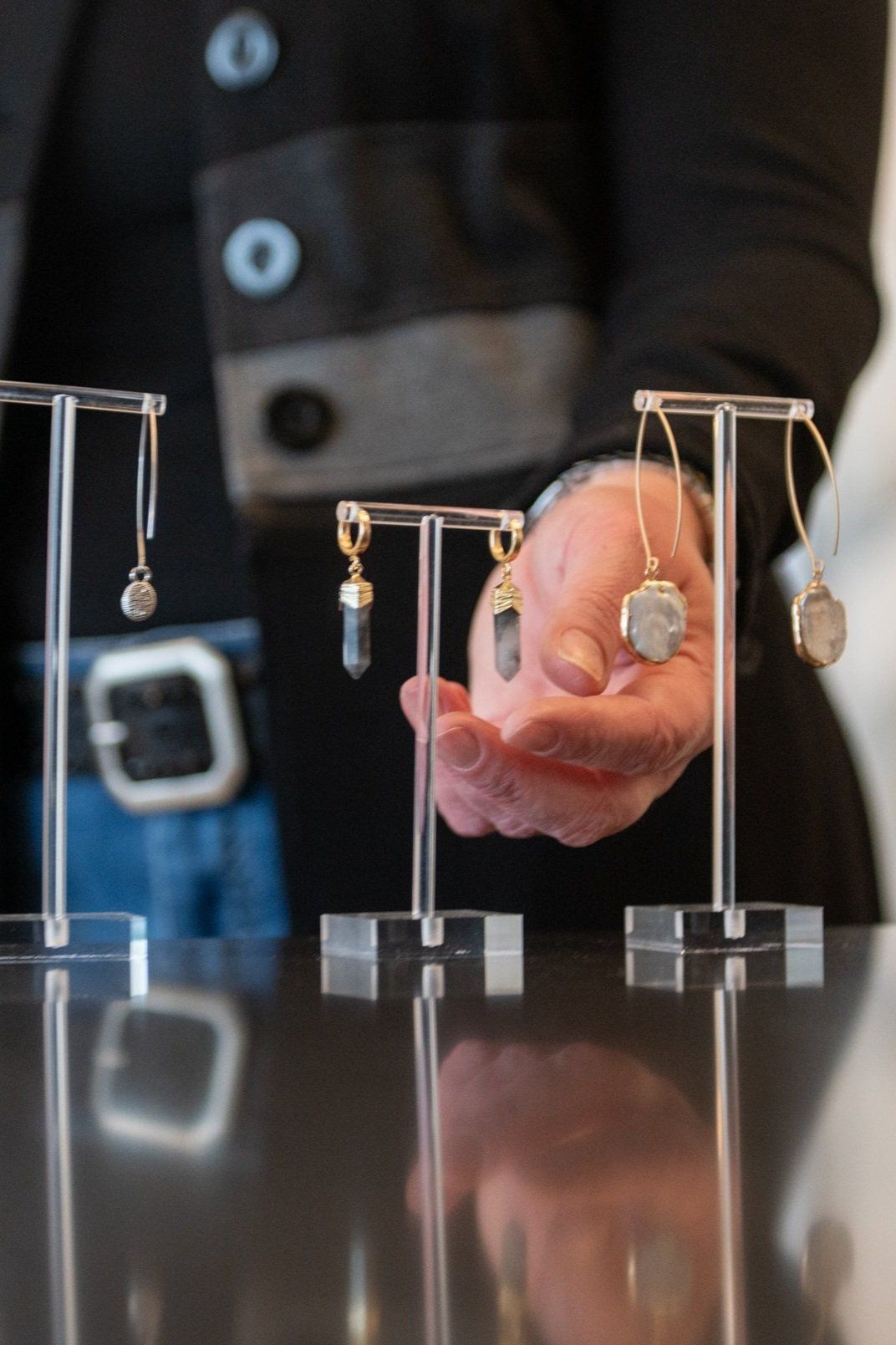 Hand holding a gold pocket watch beside small balance scales on a reflective table