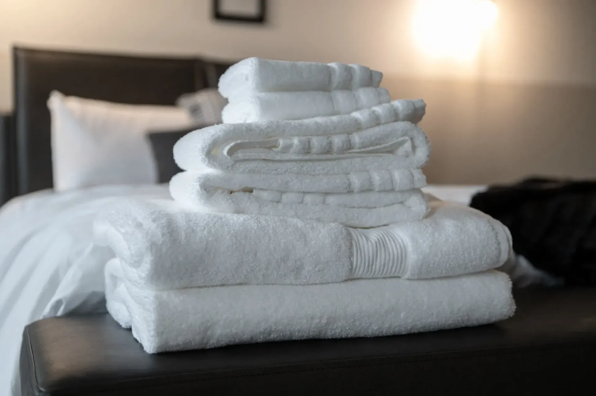 Stack of white folded towels on a bed in a softly lit bedroom