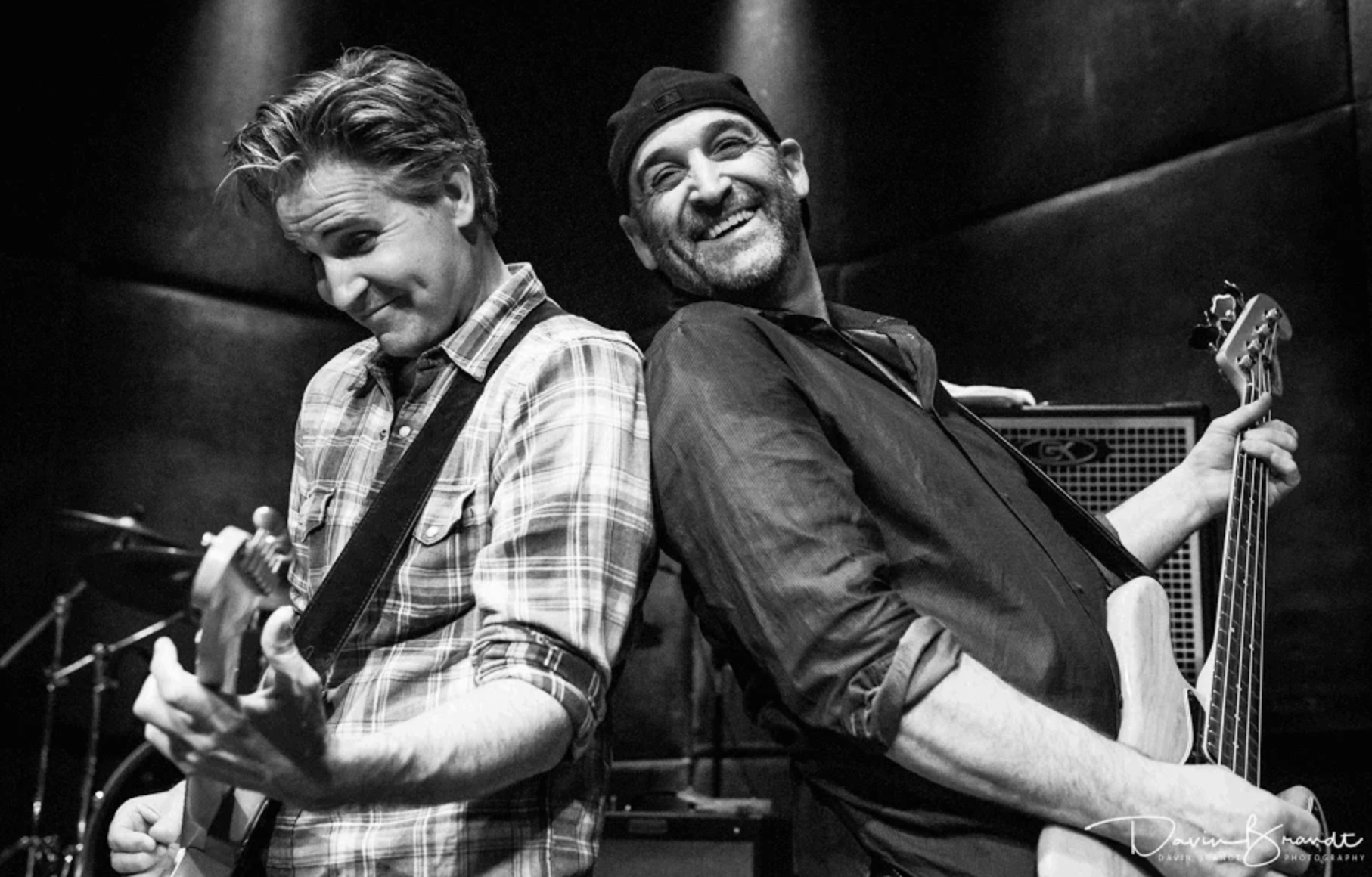 Martin Zellar and Nick Ciola guitars back-to-back on stage, smiling under dramatic lighting