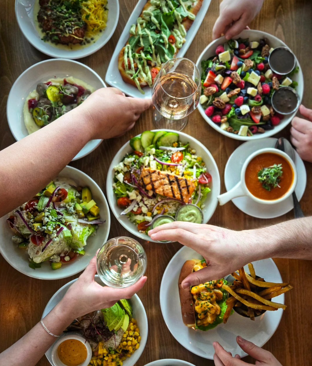 Overhead view of people sharing colorful dishes and drinks around a wooden table