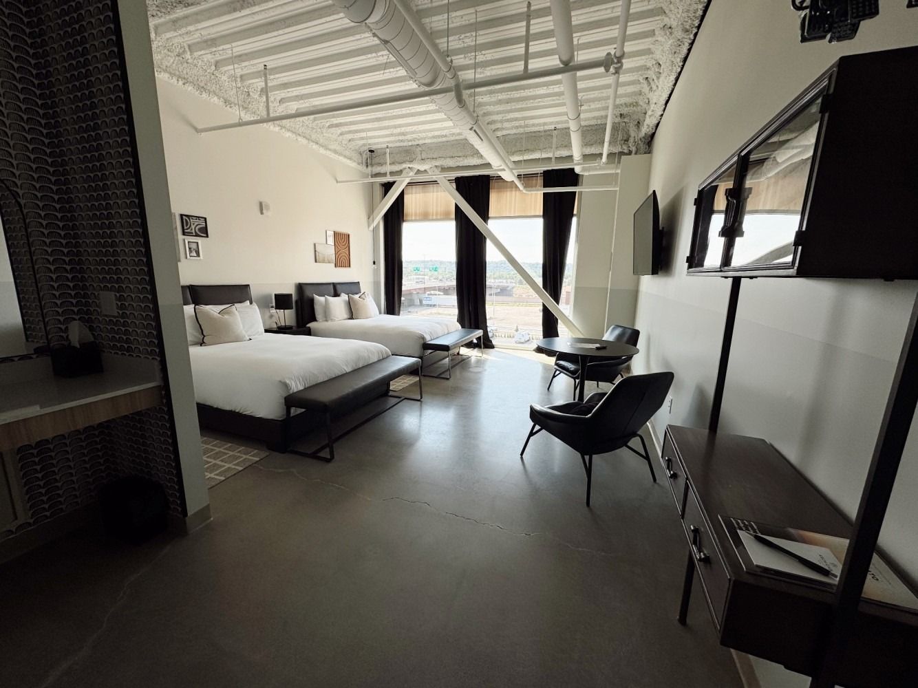 Modern loft bedroom with bed, lounge chair, and large windows overlooking a city view