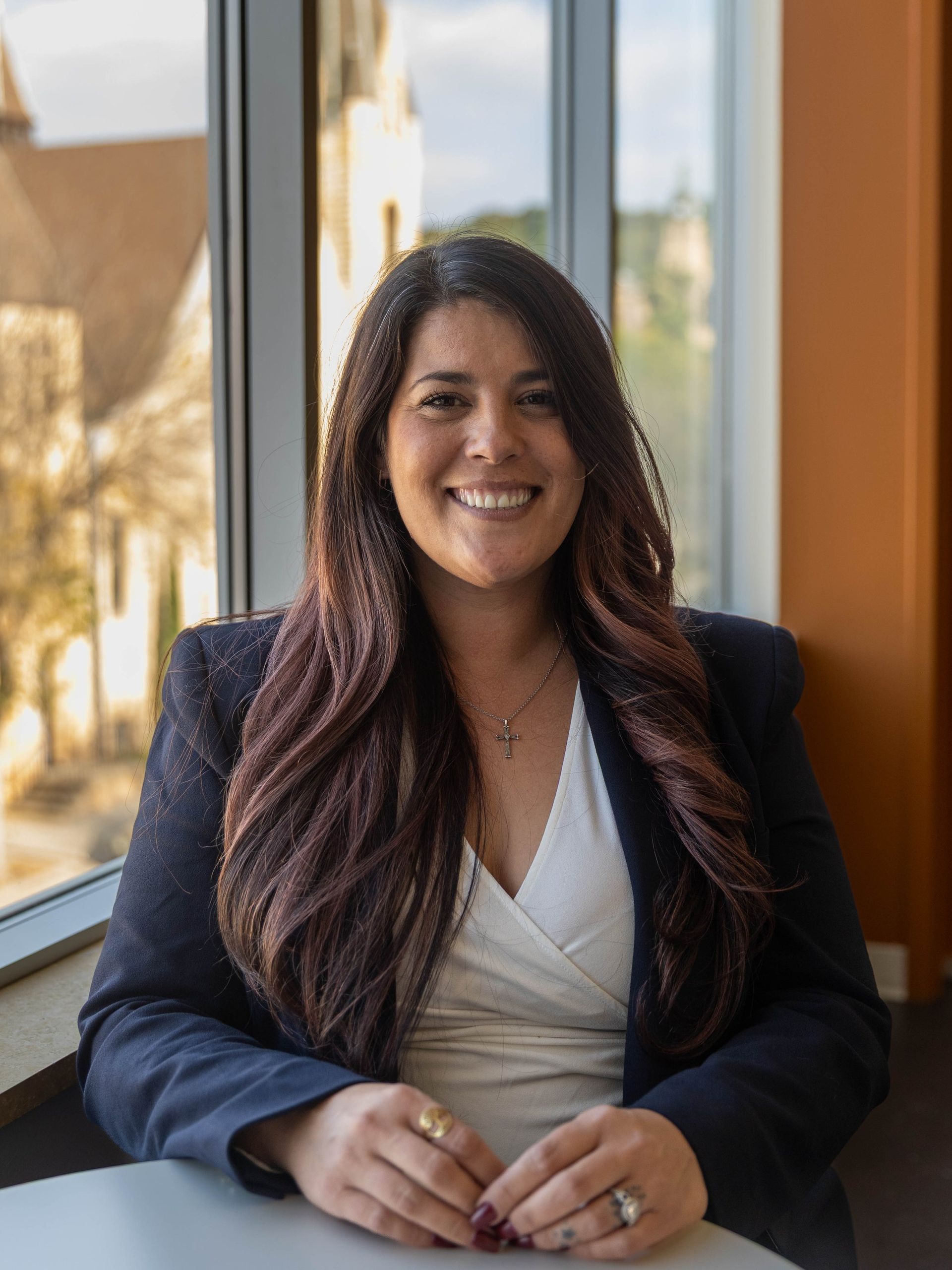 Smiling woman in a navy blazer seated by a window in a bright office