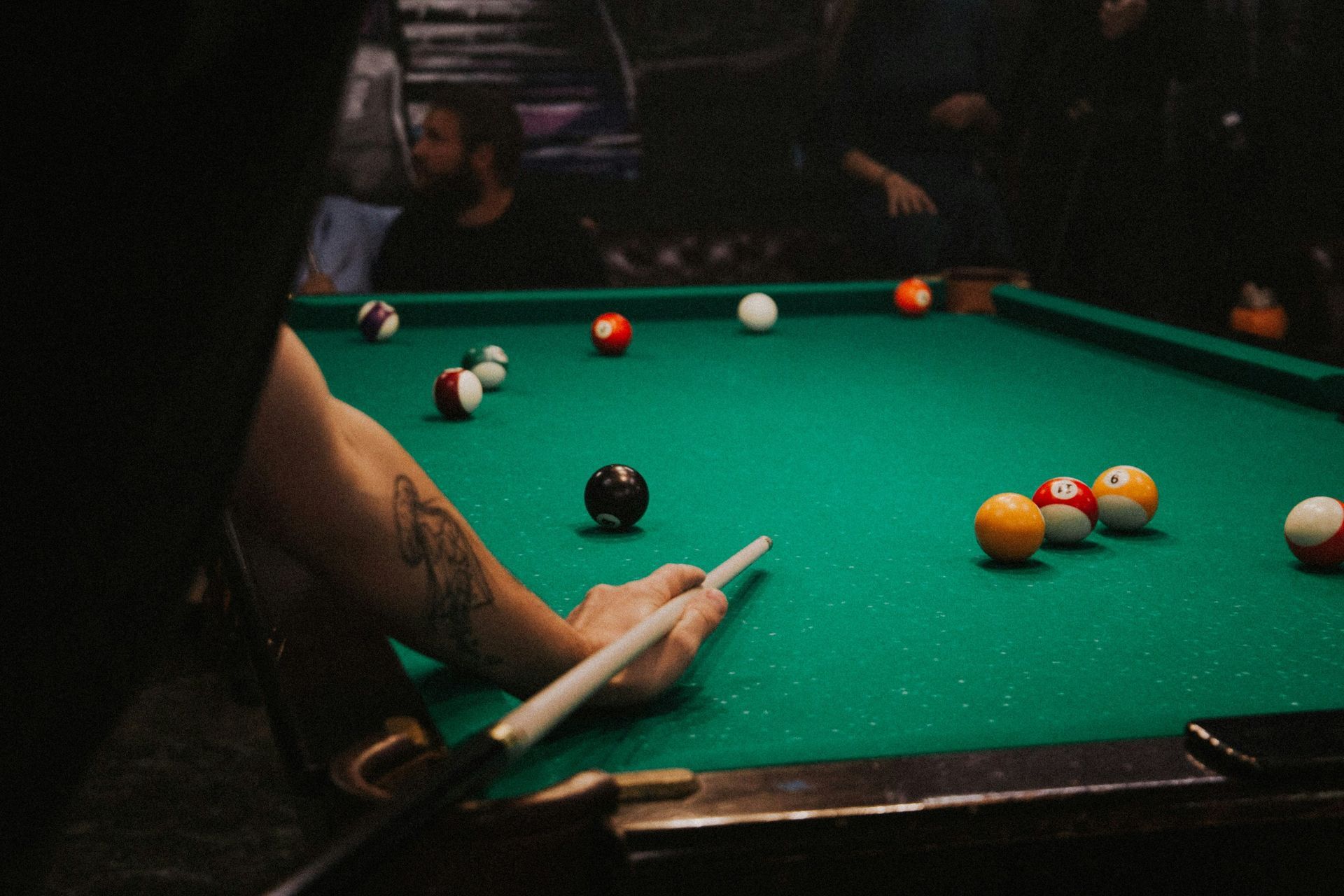 Person aiming a pool cue at billiard balls on a green pool table in a dimly lit room