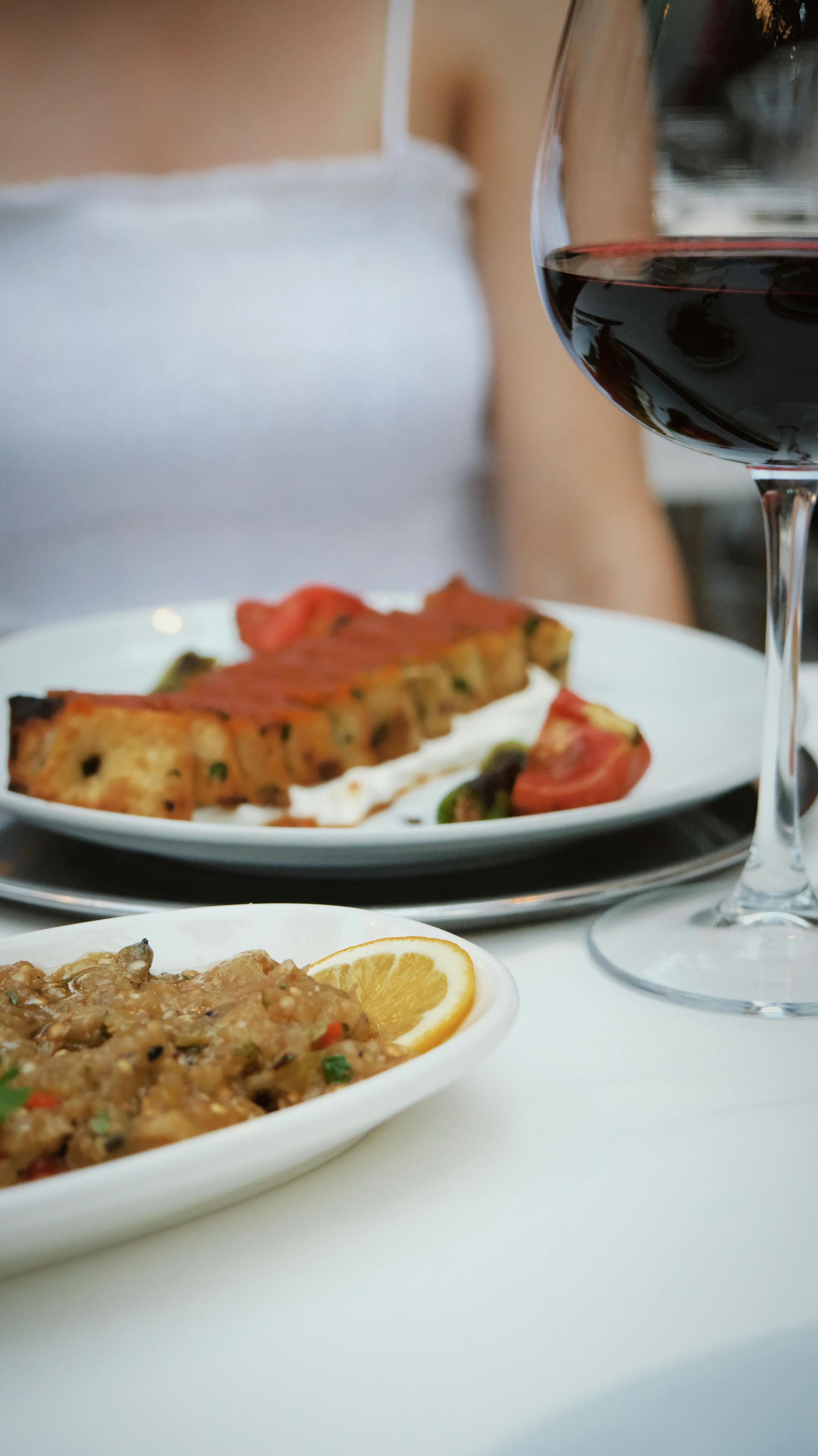 Plate of food with tomatoes and orange slice beside a glass of red wine at a dining table