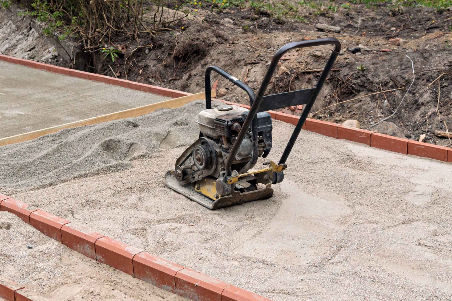 Compact plate compactor on a concrete surface beside a curb and dirt slope