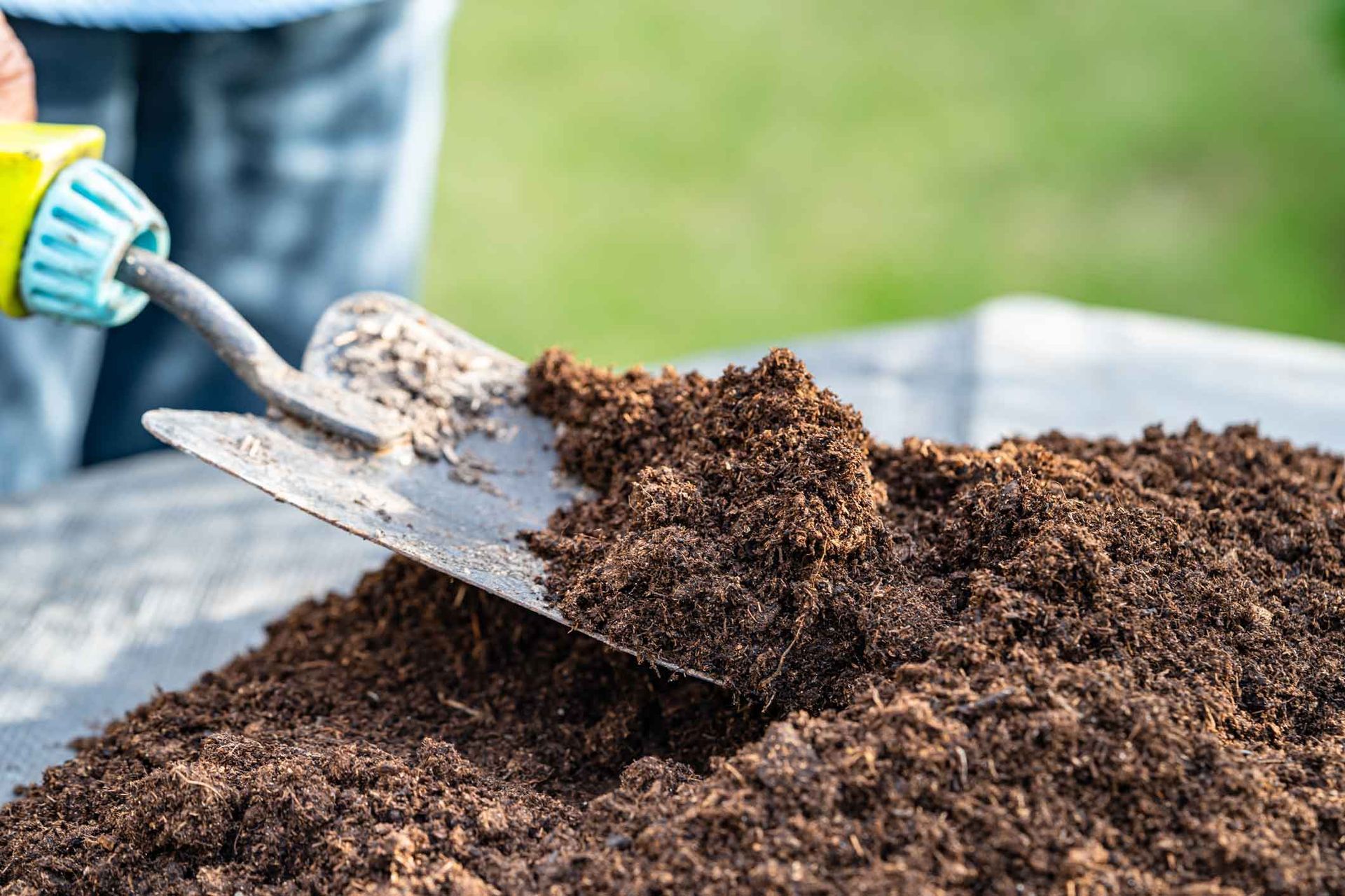 Person spreading soil with a shovel over a garden bed outdoors