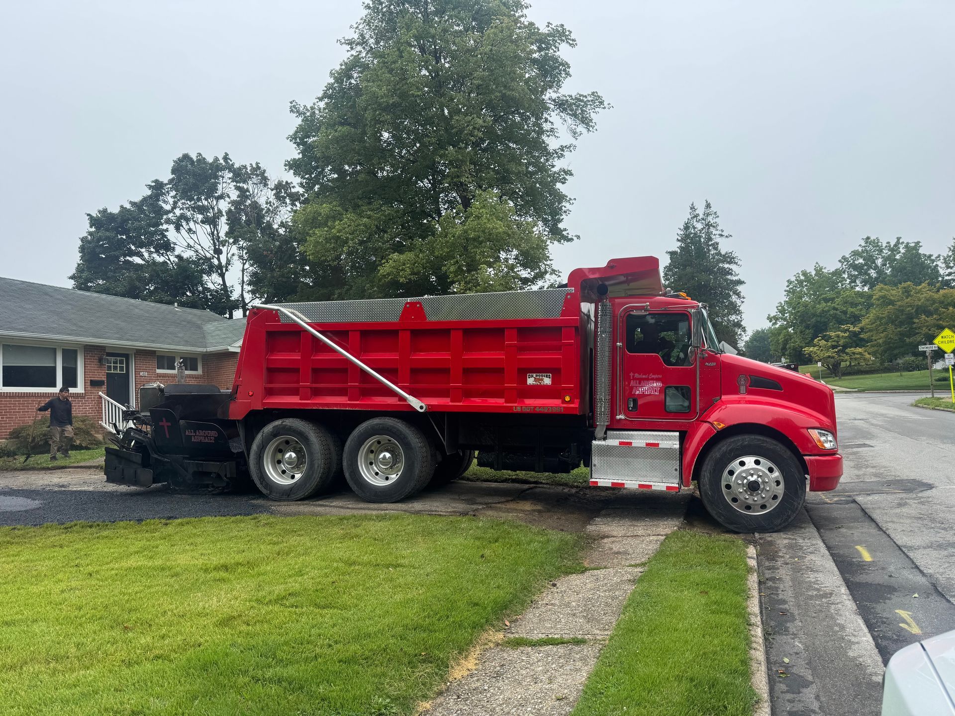 Red dump truck parked on a driveway beside a grassy lawn and sidewalk