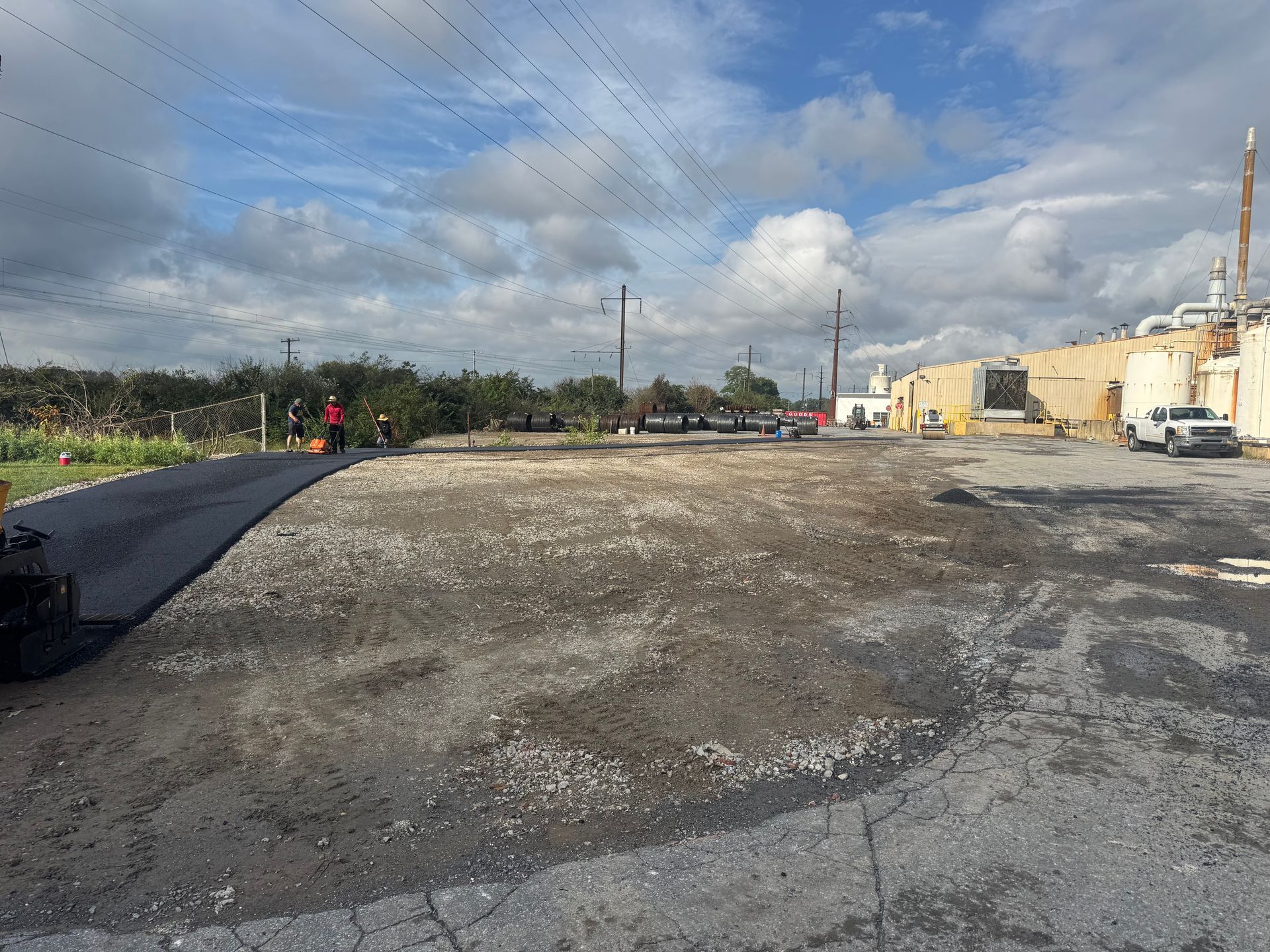 Empty gravel lot beside a road and buildings under a cloudy sky