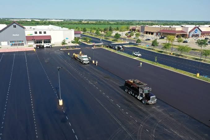 Aerial view of a parking lot repaved with fresh black asphalt and construction trucks on site