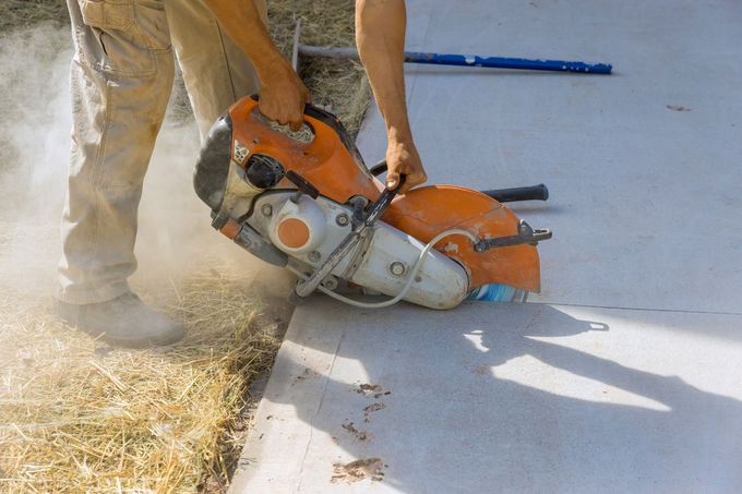 Worker cutting concrete with a circular saw, creating dust on a sunlit construction site