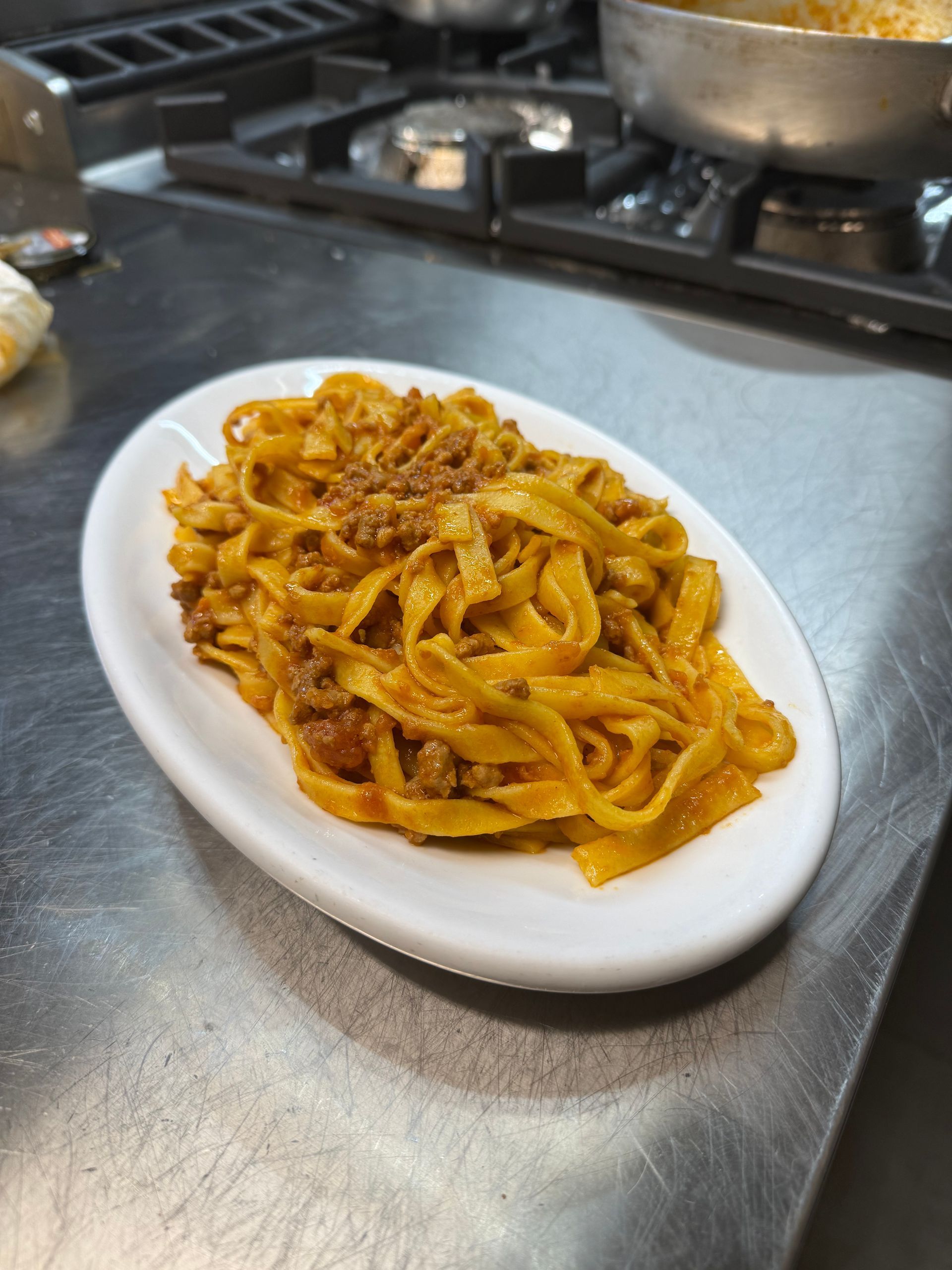 Piatto di tagliatelle al ragù su una superficie in acciaio inox vicino ai fornelli.